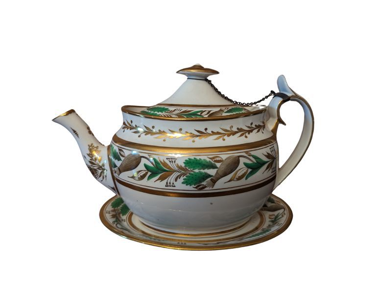 White teapot on plate, adored with gold and green pattern